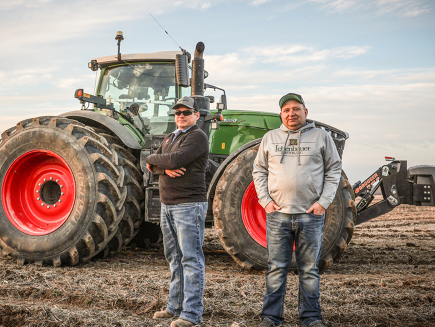Two farmers standing in a field with the Fendt tractor in the background