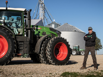 Male Farmer stands in front of Fendt tractor and grain bins