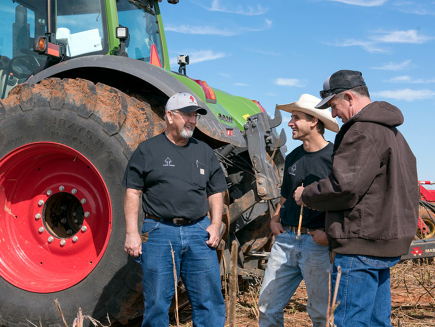 Two farmers and their dealer in front of a Fendt tractor